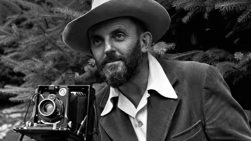 Ansel Adams portrait with large format camera, hat and beard, trees behind