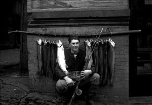 Young Eddie Bauer crouching with fishing rod and line of fish, early years